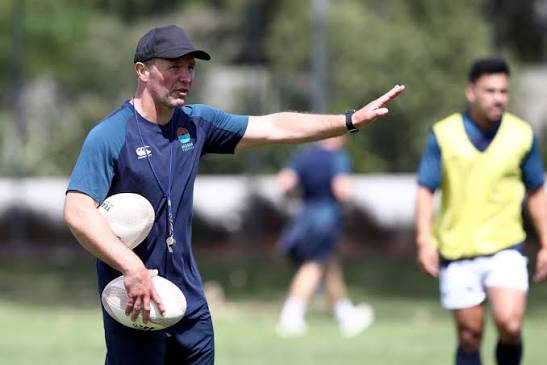 Rugby coach holding a ball and directing players during a training session, demonstrating an organised coaching environment