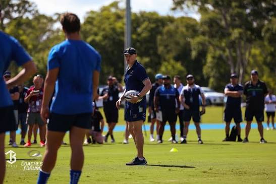 Rugby coaches gathered at a coaching forum, watching a demonstration session on a training pitch