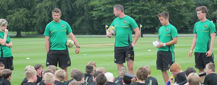 Rugby coaches addressing a group of young players at an outdoor coaching session, demonstrating a training drill
