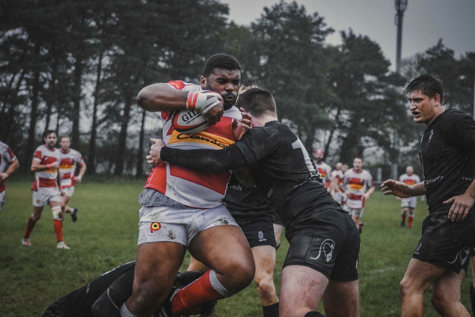 Rugby player driving through tackle in wet weather match